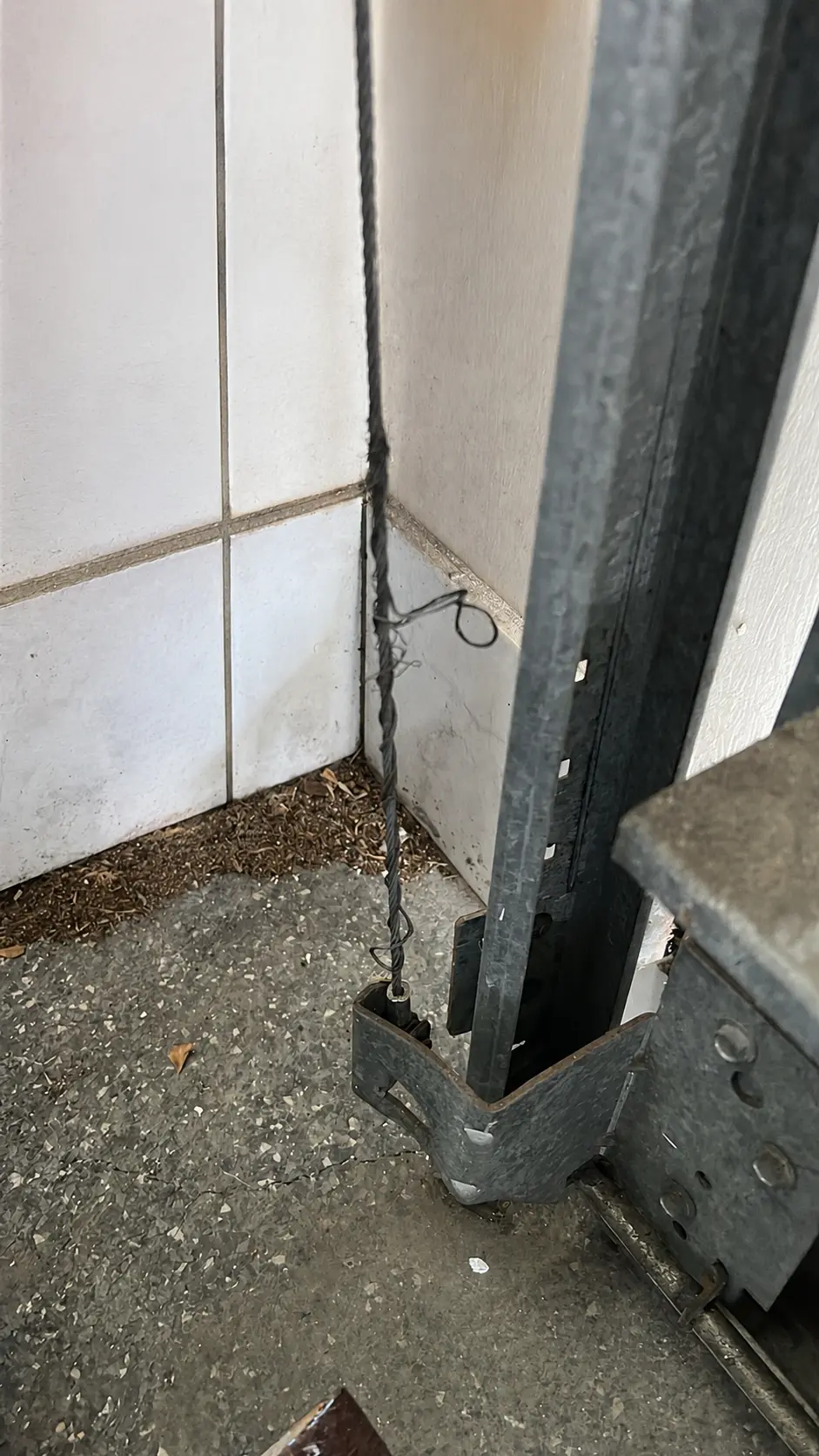 Frayed garage door cable beside a cable drum and vertical track